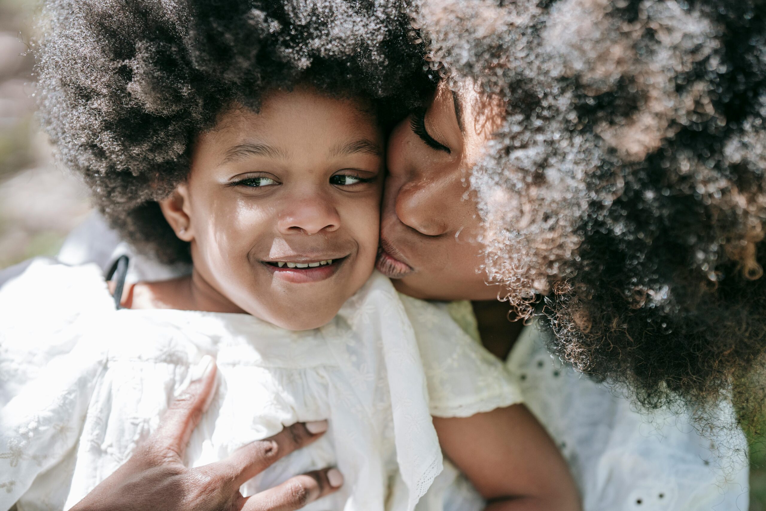 Affectionate moment between a mother and daughter with afro hair, embracing love and happiness.
